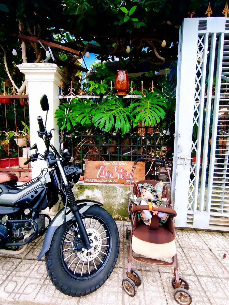 Mặt tiền Tiệm Bánh An Yên: biển gỗ, cây monstera, xe máy và xe đẩy em bé.